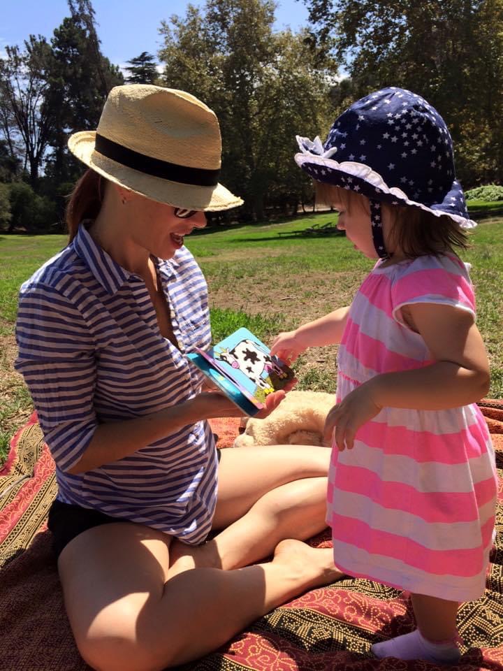 Mother reading a book to her young daughter outdoors, encouraging speech development.